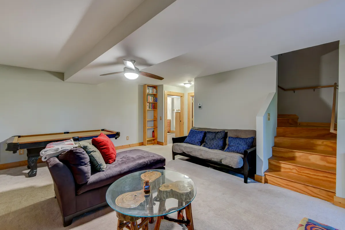 A view of the recreation room with a pool table, comfortable seating, a coffee table, and a staircase leading to other parts of the home. The arrangement suggests a space where players and spectators can relax together, perfect for family game nights.