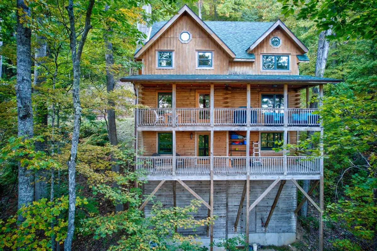This image showcases the exterior of Hideaway Homestead, highlighting its wooden structure with multiple balconies surrounded by lush trees. The calm lighting suggests either sunrise or sunset, emphasizing the home's integration with its natural surroundings. The balconies offer clear vantage points for observing the changing seasons and local wildlife.