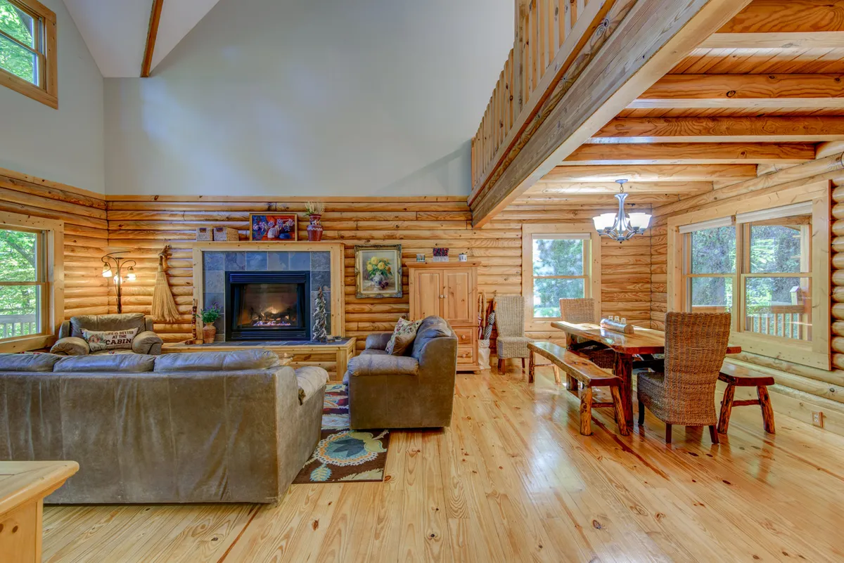 A spacious open living area with a prominent fireplace, comfortable sofas, a large dining table, and expansive windows that let in abundant natural light. The room feels inviting, ideal for family gatherings and cozy evenings by the fire.