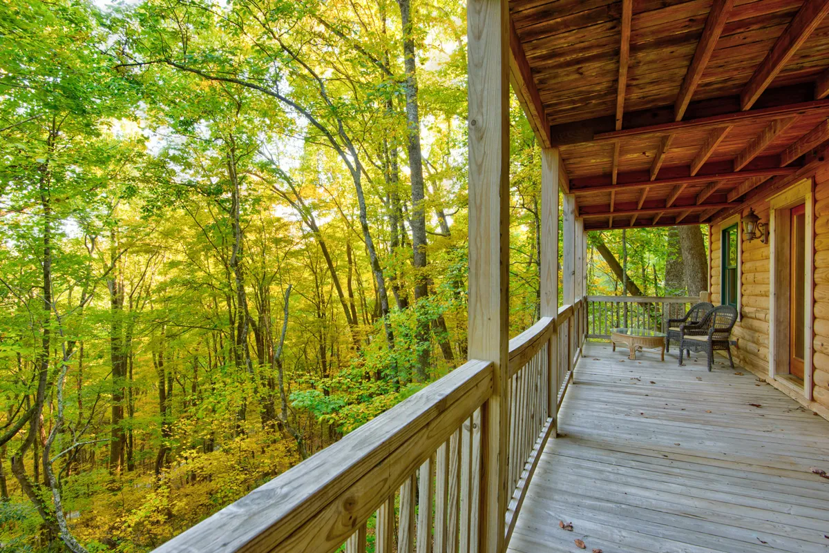 A peaceful wooden deck with rustic furniture, wooden railing, and trees encircling the porch. The deck is well-appointed for relaxation, offering clear sightlines into the forest, ideal for wildlife spotting, enjoying sunsets, or birdwatching.