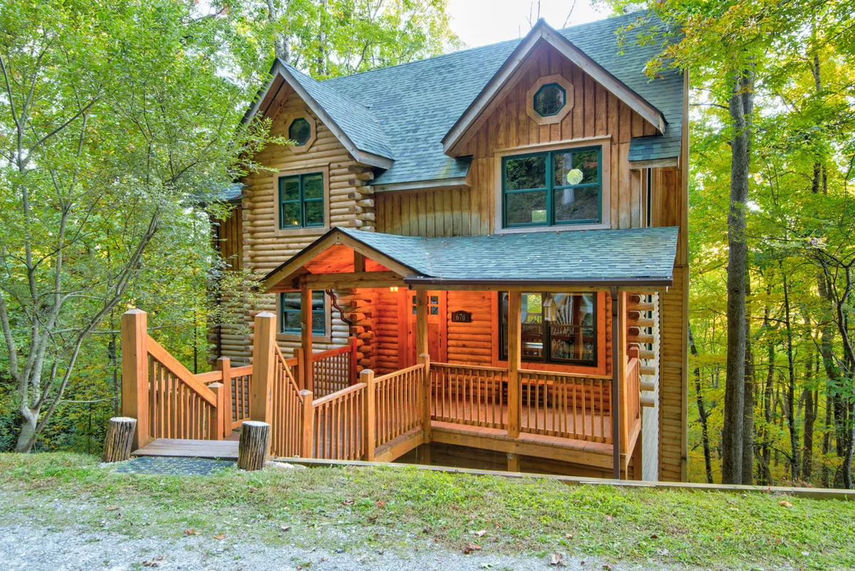 The image showcases a charming log cabin nestled among tall trees, with a spacious wooden porch facing the forest. Soft evening light bathes the cabin, highlighting the inviting porch where guests can gather, relax, or enjoy a cup of coffee while surrounded by nature.