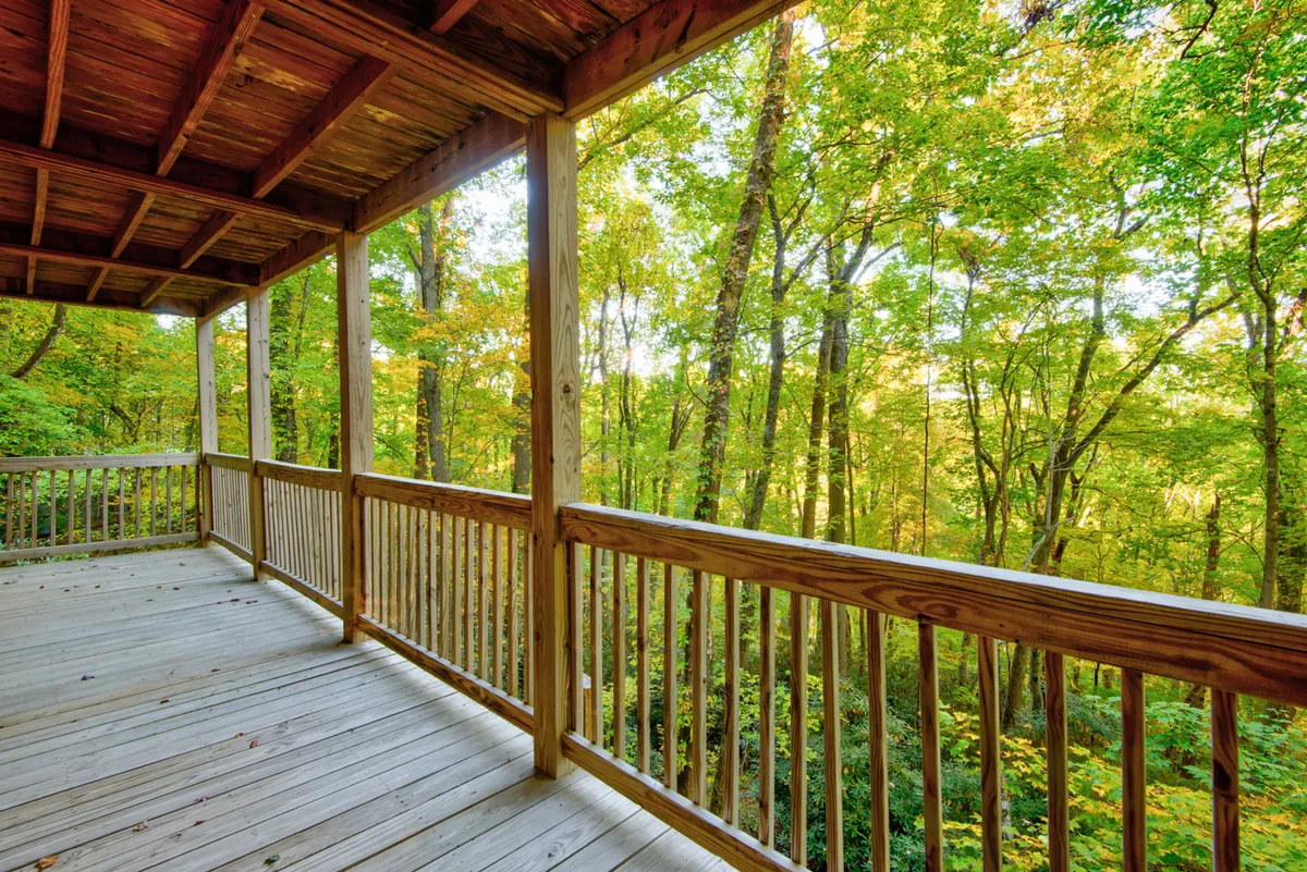 A view from the deck with wooden railing and floor, overlooking dense greenery. The natural light and view of the forest make it an inviting spot to unwind while staying connected to nature.