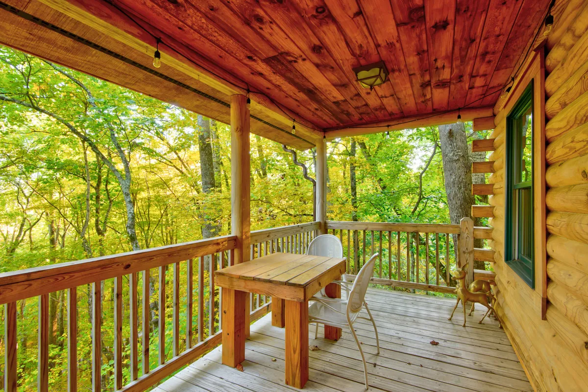 An exterior shot of a wooden table and white chair set amidst surrounding greenery. The scene exudes tranquility, suggesting an ideal spot for outdoor dining, morning coffee, or relaxed conversation in nature.